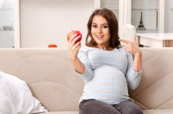 Young pregnant woman sitting on the sofa at home 