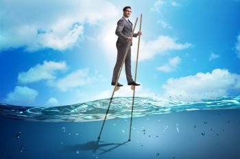 Businessman walking on stilts in water sea