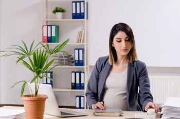 Young pregnant employee working in the office 