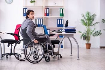 Young handsome employee in wheelchair working in the office  