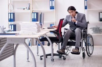 Young handsome employee in wheelchair working in the office  