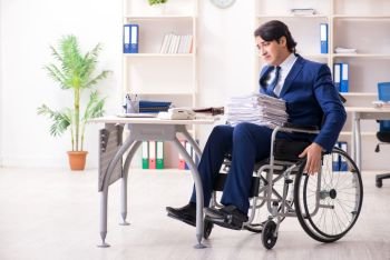 The young male employee in wheelchair working in the office . Young male employee in wheelchair working in the office 