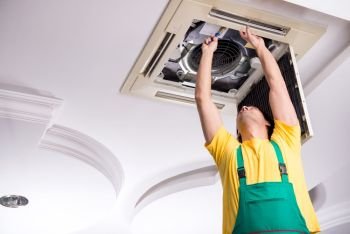 The young repairman repairing ceiling air conditioning unit . Young repairman repairing ceiling air conditioning unit 