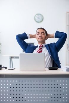 The young male businessman sitting in the office . Young male businessman sitting in the office 