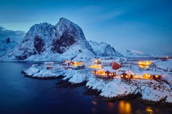 Famous tourist attraction Hamnoy fishing village on Lofoten Islands, Norway with red rorbu houses in winter snow illuminated in the evening. Hamnoy fishing village on Lofoten Islands, Norway 