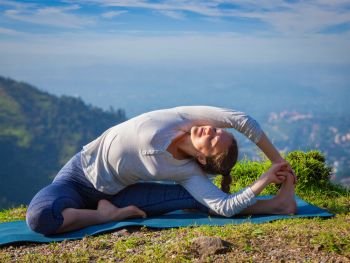Yoga outdoors - young sporty fit woman doing Hatha Yoga asana parivritta janu sirsasana - Revolved Head-to-Knee Pose - in mountains in the morning. Young sporty fit woman doing Hatha Yoga asana