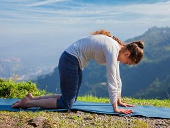 Yoga exercise outdoors - sporty fit woman practices yoga asana Marjariasana - cat pose outdoors in Himalayas. Sporty fit woman practices yoga asana Marjariasana outdoors
