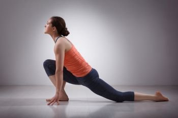 Beautiful sporty fit yogini woman practices yoga asana  Anjaneyasana - low crescent lunge pose in surya namaskar in studio. Fit yogini woman practices yoga asana  Anjaneyasana
