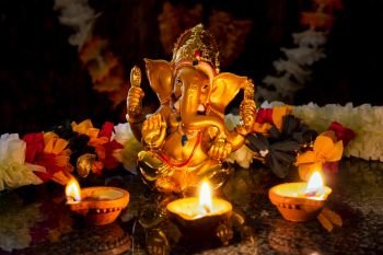Ganesh Chaturthi or Diwali concept - Ganesha  figurine with Diwali lights oil ghee candles,  India. Ganesha with Diwali lights