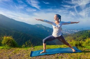Yoga outdoors - sporty fit woman doing yoga asana Virabhadrasana 2 - Warrior pose posture outdoors in Himalayas mountains in the morning. Woman doing yoga asana Virabhadrasana 2 - Warrior pose outdoors