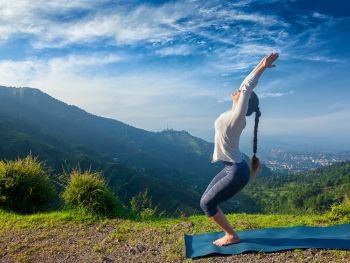 Young sporty fit woman doing yoga asana Utkatasana (chair pose) outdoors in mountains Himalayas in the morning. Himachal Pradesh, India. Woman doing yoga asana Utkatasana outdoors