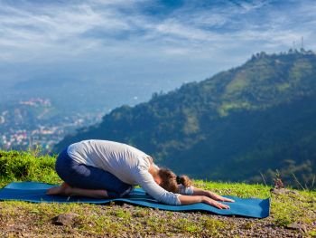 Sporty fit woman practices yoga asana Balasana - child pose outdoors in mountains. Sporty fit woman practices yoga asana Balasana
