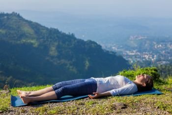 Woman relaxes in yoga asana Savasana - corpse pose outdoors in Himalayas. Himachal Pradesh, India. Woman relaxes in yoga asana Savasana outdoors