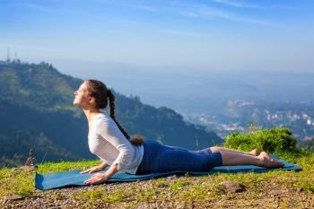 Beautiful sporty fit woman practices yoga asana bhujangasana - cobra pose beginner variation outdoors in mountains in the morning. Woman practices yoga asana bhujangasana cobra pose