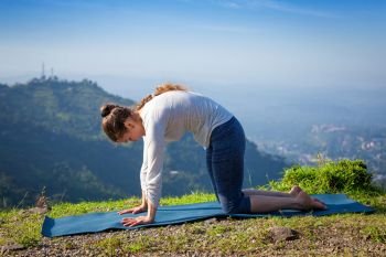 Sporty fit woman practices yoga asana Marjariasana - cat pose outdoors in Himalayas. Woman practices yoga asana Marjariasana outdoors