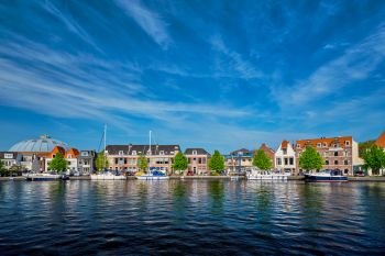 Boats and houses on Spaarne river with blue sky. Haarlem, Netherlands. Boats and houses on Spaarne river. Haarlem, Netherlands