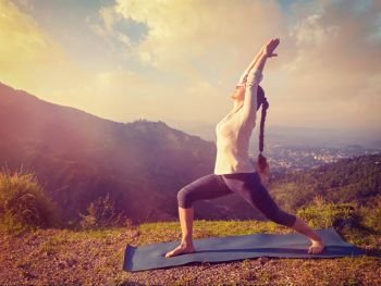 Yoga outdoors - sporty fit woman doing yoga asana Virabhadrasana 1 - Warrior pose posture outdoors in Himalayas mountains in the morning. Vintage retro effect filtered hipster style image.. Woman doing yoga asana Virabhadrasana 1 - Warrior pose outdoors