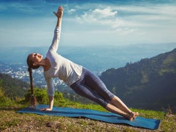 Yoga outdoors - beautiful sporty fit woman doing yoga asana Vasisthasana - side plank pose in mountains. Vintage retro effect filtered hipster style image.. Woman doing yoga asana Vasisthasana - side plank pose outdoors
