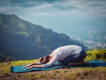 Sporty fit woman practices yoga asana Balasana - child pose outdoors in mountains. Vintage retro effect filtered hipster style image.. Sporty fit woman practices yoga asana Balasana
