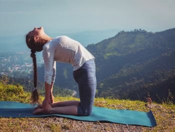 Yoga - outdoors  young beautiful slender woman yoga instructor doing camel pose Ustrasana asana exercise outdoors in mountains in the morning. Vintage retro effect filtered hipster style image.. Woman doing yoga asana Ustrasana camel pose outdoors