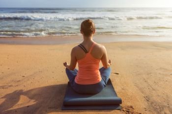 Woman doing yoga - meditating and relaxing in Padmasana Lotus Pose outdoors at tropical beach on sunset. Woman doing yoga Lotus pose oudoors at beach
