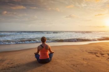 Woman doing yoga - meditating and relaxing in Padmasana Lotus Pose outdoors at tropical beach on sunset. Woman doing yoga Lotus pose oudoors at beach