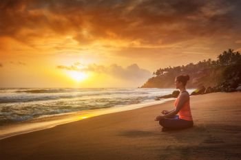 Young sporty fit woman doing yoga - meditating and relaxing in Padmasana Lotus Pose) with chin mudra outdoors at tropical beach on sunset. Young sporty fit woman doing yoga oudoors at beach