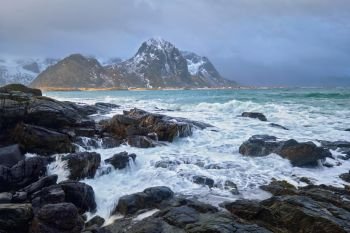 Waves crushing on rocks on rocky coast of fjord of Norwegian sea in winter. Lofoten islands, Norway. Rocky coast of fjord in Norway