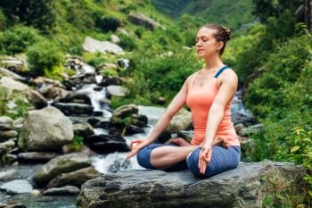 Woman meditate in Hatha yoga asana Padmasana outdoors at tropical waterfall. Woman in Padmasana outdoors