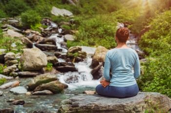 Woman meditate in Hatha yoga asana Padmasana outdoors at tropical waterfall. Yoga outdoors - Padmasana asana lotus pose
