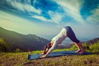 Vintage retro hipster effect image of woman in yoga asana Adho mukha svanasana - downward facing dog - Surya Namaskar Sun Salutation in Himalayas in the morning. Young sporty fit woman doing yoga oudoors in mountains