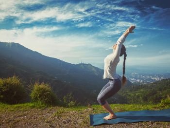 Vintage retro effect hipster style image of young sporty fit woman doing yoga asana Utkatasana (chair pose) outdoors in mountains Himalayas in the morning. Himachal Pradesh, India. Woman doing yoga asana Utkatasana outdoors
