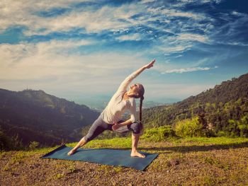 Vintage retro effect hipster style image of sporty fit woman practices yoga asana Utthita Parsvakonasana -  extended side angle pose outdoors in mountains in the  morning. Woman practices yoga asana Utthita Parsvakonasana outdoors