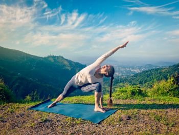 Vintage retro effect hipster style image of sporty fit woman practices yoga asana Utthita Parsvakonasana -  extended side angle pose outdoors in mountains in the  morning. Woman practices yoga asana Utthita Parsvakonasana outdoors