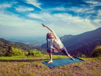 Vintage retro effect hipster style image of sporty fit woman practices yoga asana Utthita Parsvakonasana - extended side angle pose outdoors in mountains in the morning. Woman practices yoga asana Utthita Parsvakonasana outdoors