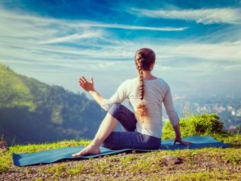 Vintage retro effect hipster style image of sporty fit woman practices yoga asana Parivrtta Marichyasana -  seated spinal twist outdoors in mountains in the  morning. Woman practices yoga asana Marichyasana 