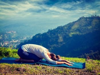 Vintage retro effect hipster style image of sporty fit woman practices yoga asana Balasana - child pose outdoors in mountains. Sporty fit woman practices yoga asana Balasana