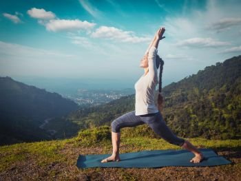 Yoga outdoors - sporty fit woman doing yoga asana Virabhadrasana 1 - Warrior pose posture outdoors in Himalayas mountains in the morning. Vintage retro effect filtered hipster style image.. Woman doing yoga asana Virabhadrasana 1 - Warrior pose outdoors