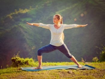 Yoga outdoors - sporty fit woman doing yoga asana Virabhadrasana 2 - Warrior pose posture outdoors in Himalayas mountains in the morning. Vintage retro effect filtered hipster style image.. Woman doing yoga asana Virabhadrasana 2 - Warrior pose outdoors
