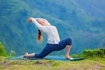 Yoga outdoors - sporty fit woman practices Hatha yoga asana Anjaneyasana - low crescent lunge pose posture outdoors in Himalayas mountains. Sporty fit woman practices yoga asana Anjaneyasana in mountains