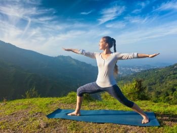 Yoga outdoors - sporty fit woman doing yoga asana Virabhadrasana 2 - Warrior pose posture outdoors in Himalayas mountains in the morning. Woman doing yoga asana Virabhadrasana 2 - Warrior pose outdoors
