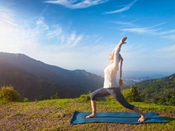 Yoga outdoors - sporty fit woman doing yoga asana Virabhadrasana 1 - Warrior pose posture outdoors in Himalayas mountains in the morning. Woman doing yoga asana Virabhadrasana 1 - Warrior pose outdoors