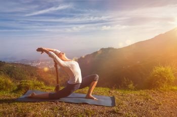 Yoga outdoors - sporty fit woman practices yoga Anjaneyasana - low crescent lunge pose outdoors in mountains in morning. With light leak and lens flare. Sporty fit woman practices yoga Anjaneyasana in mountains