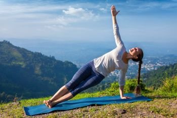 Yoga outdoors - beautiful sporty fit woman doing yoga asana Vasisthasana - side plank pose in mountains. Woman doing yoga asana Vasisthasana - side plank pose outdoors