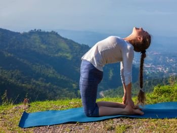 Yoga - outdoors young beautiful slender woman yoga instructor doing camel pose Ustrasana asana exercise outdoors in mountains in the morning. Woman doing yoga asana Ustrasana camel pose outdoors
