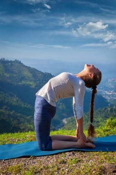 Yoga - outdoors  young beautiful slender woman yoga instructor doing camel pose Ustrasana asana exercise outdoors in mountains in the morning. Woman doing yoga asana Ustrasana camel pose outdoors
