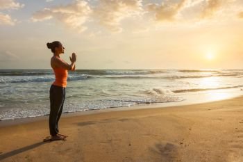 Woman doing Ashtanga Vinyasa Yoga asana Tadasana Samasthiti yoga posture on beach on sunset. Woman doing yoga on beach
