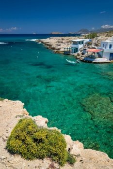 Greece scenic island view - small harbor with fishing boats in crystal clear turquoise water, traditishional whitewashed house. MItakas village, Milos island, Greece.. Crystal clear blue water at MItakas village beach, Milos island, Greece.