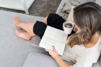 Beautiful young woman relaxing at home reading a book