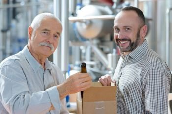 portrait of men in brewery holding box of bottled beer